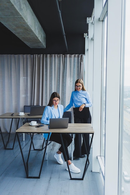 Donne d'affari impegnate con un laptop in ufficio che guardano i contenuti sul laptop e discutono del progetto insieme seduti in ufficio durante una pausa di lavoro Discussione aziendale sul lavoro di squadra