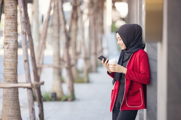 Donne di affari arabe in hijab che tiene un caffè in strada e che tiene un telefono cellulare
