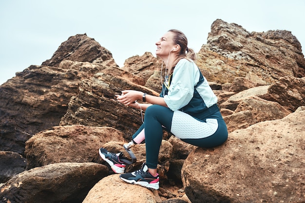 Donne disabili semplicemente sorridenti e sorridenti in abbigliamento sportivo con protesi alle gambe sedute sui massi