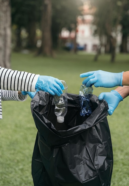 Donne e uomini conservano le bottiglie di plastica dei rifiuti in sacchi neri al parco alla luce del mattino