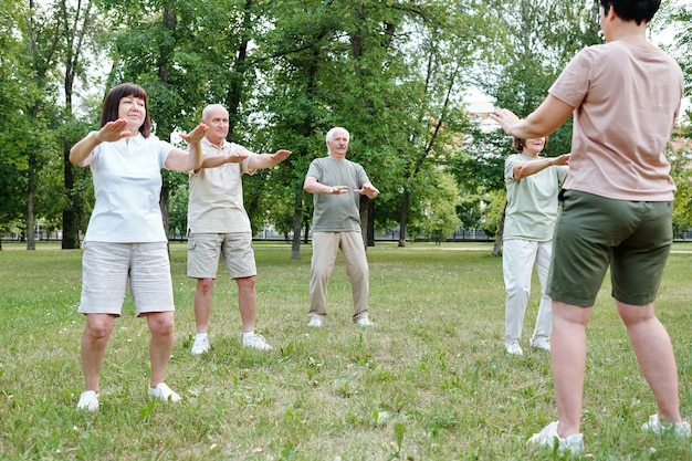 Donne e uomini maturi che fanno esercizi insieme all'allenatore nel parco