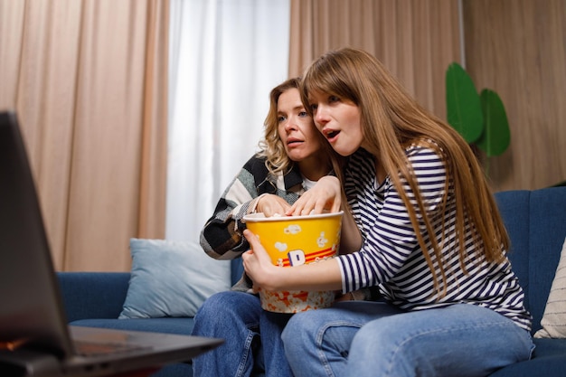 Donne eccitate di età diverse che guardano film spaventosi e mangiano popcorn a casa sul divano