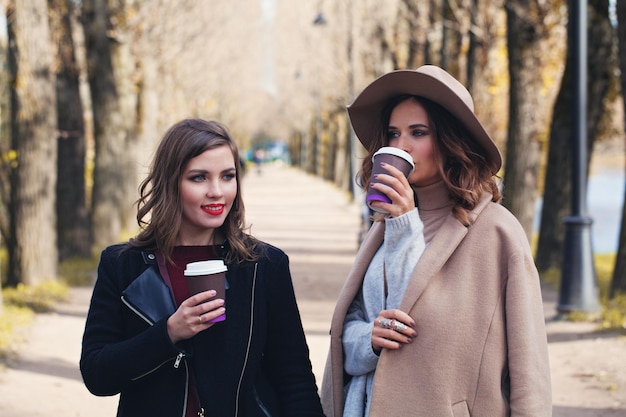 Donne felici che bevono caffè per andare all'aperto nel parco autunnale