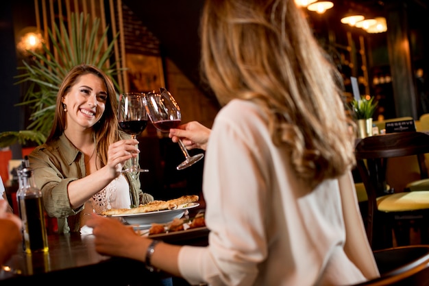 Donne felici che bevono vino rosso al ristorante durante la cena leggera