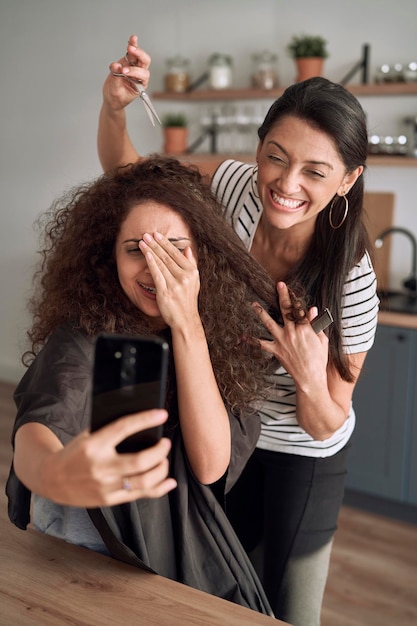 Donne felici che fanno selfie divertenti mentre si tagliano i capelli