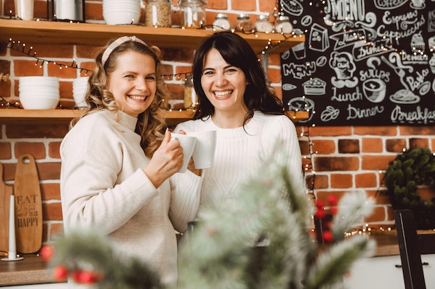 Donne felici e allegre che parlano e bevono caffè a casa in cucina. bionda e bruna si parlano