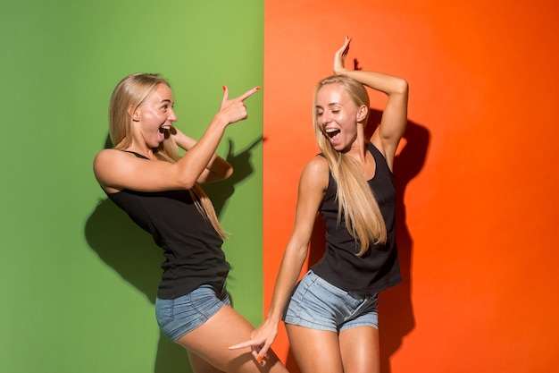 Donne felici in piedi e sorridenti isolate su sfondo per studio. Bellissimo ritratto femminile a mezzo busto. Giovani donne emotive. Le emozioni umane, concetto di espressione facciale. Vista frontale.