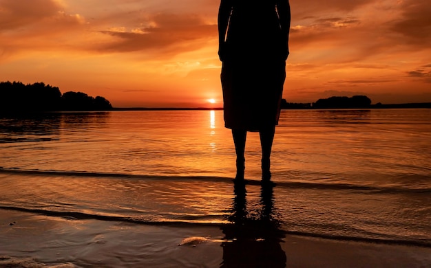 Donne gambe piedi silhouette in piedi in acqua al tramonto sul lago