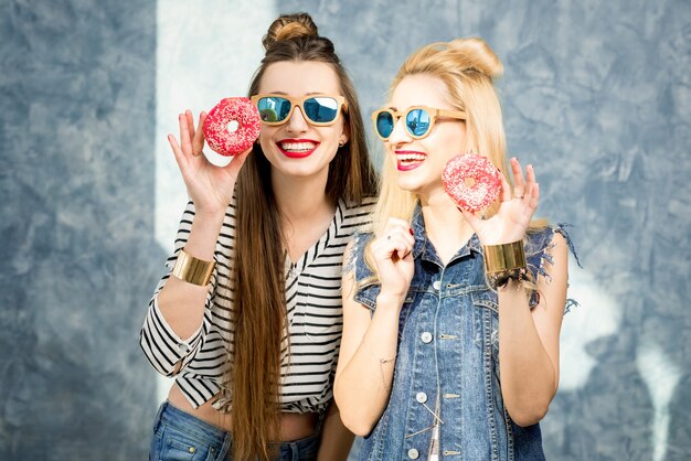 Donne giocose che si divertono con ciambelle dolci sullo sfondo blu della parete