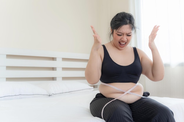 Donne grasse asiatiche Ragazza grassa Chubby sovrappeso infelice misurando la sua vita in camera da letto Concetto di problema di sovrappeso stile di vita dieta donna