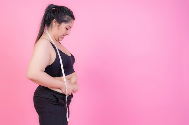 Donne grasse asiatiche Ragazza grassa Paffuto sovrappeso spremere il grasso della pancia con metro a nastro sul collo su sfondo rosa Concetto di problema di sovrappeso stile di vita dieta donna