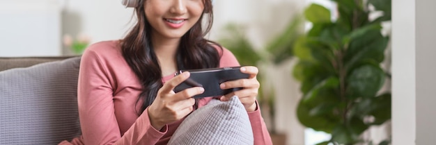 Donne in cuffia che giocano ai videogiochi sullo smartphone mentre si divertono sul divano nello stile di vita di casa