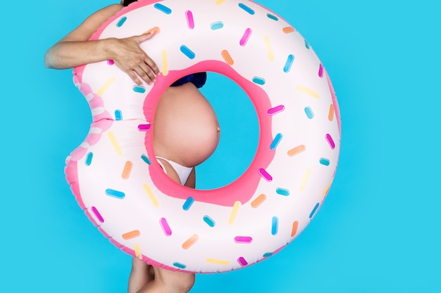 Donne incinte felici in costume da bagno con la ciambella dell'anello di nuoto su una parete blu colorata