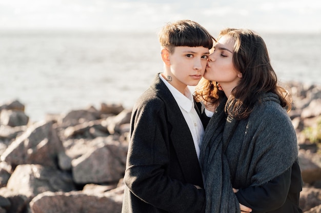 Donne lesbiche che si baciano in piedi su una roccia contro il mare e il cielo