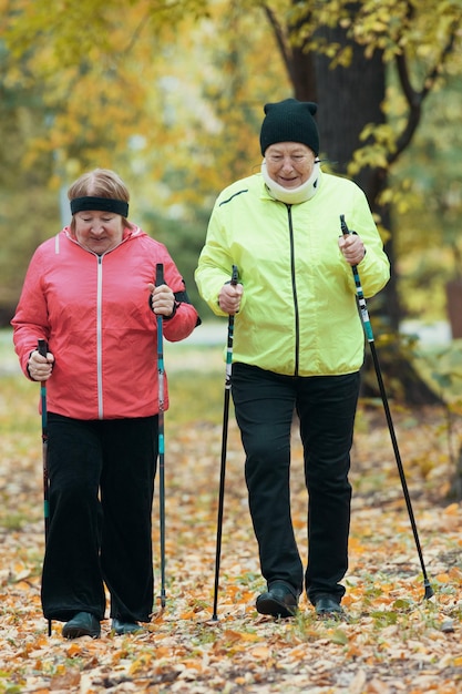 Donne mature che camminano in un parco autunnale durante una passeggiata scandinava cadono