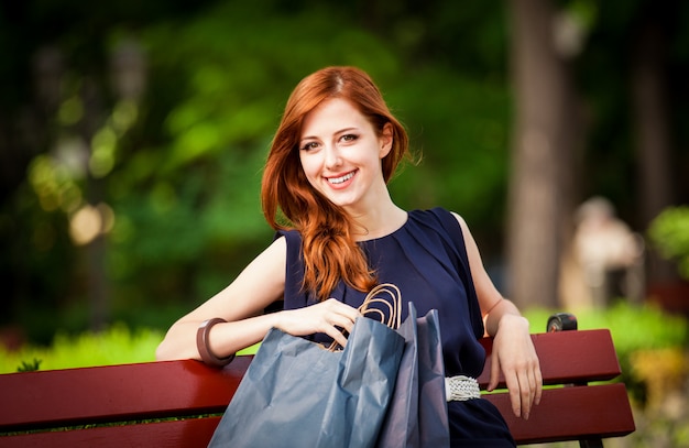 Donne rosse di stile che si siedono sul banco con i sacchetti della spesa