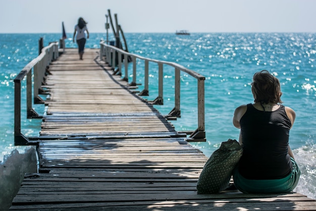 donne sedute da sole su un ponte di legno sul mare