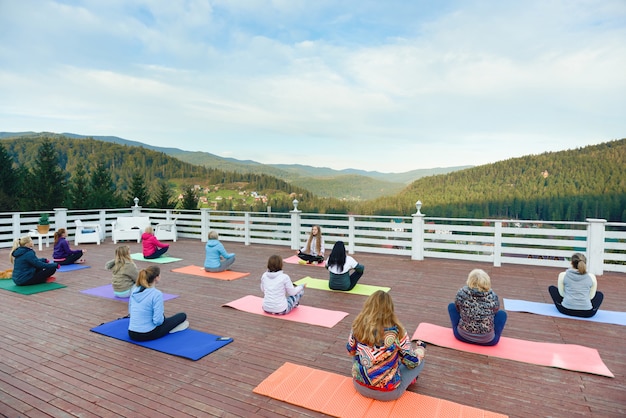 Donne sedute su stuoie di yoga in montagna, praticando.