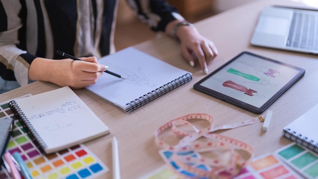 Donne stiliste che guardano i dettagli sul tablet e disegnano vestiti per una nuova collezione creativa