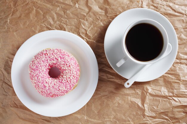 Donut rosa con sprinkle e una tazza di caffè su sfondo di carta arrugginito vista dall'alto