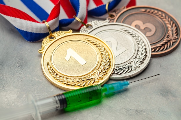 Doping per gli atleti. Medaglia d'oro, d'argento e di bronzo e siringa dopante su una superficie grigia.