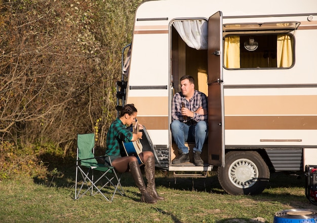 Dopo un lungo viaggio coppia rilassante in montagna. Donna che suona la chitarra. Camper retrò.