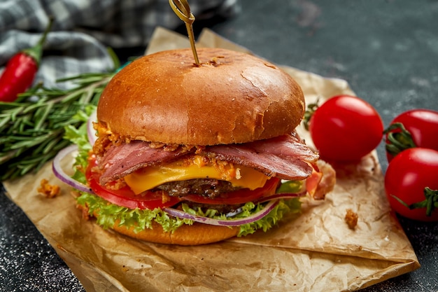 Doppio hamburger succoso con carne di manzo, pomodori pancetta, formaggio e cipolle croccanti su un tavolo scuro.