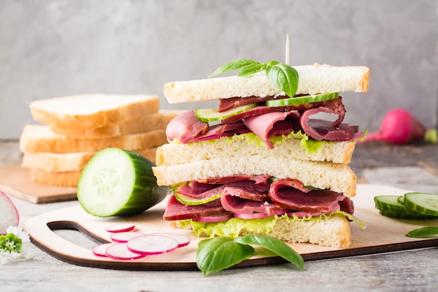 Doppio panino con pastrami, cetriolo, ravanello e basilico su un tagliere. Spuntino americano. Stile rustico.