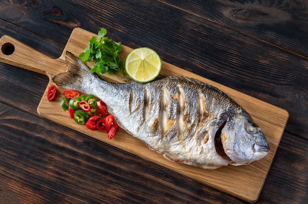 Dorada alla griglia con peperoncino, coriandolo fresco e lime sulla tavola di legno