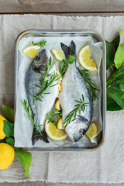 Dorado di mare crudo e fresco, pesce dorada con limone, rosmarino, origano, erbe aromatiche, olio d'oliva sul tavolo della cucina. Vista dall'alto, sfondo piatto