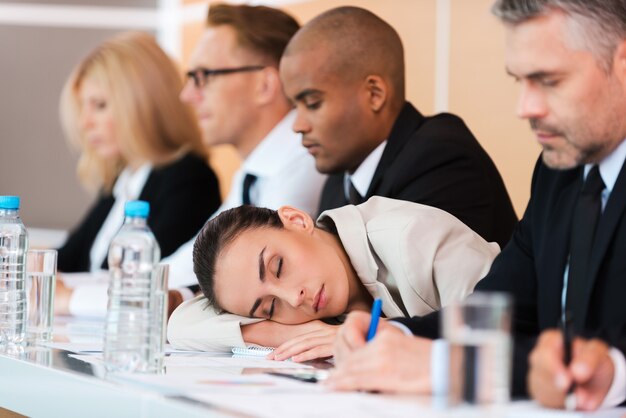 Dormire alla conferenza. Donna d'affari stanca che dorme mentre è seduta al tavolo con i suoi colleghi