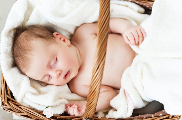 Dormire in un cestino. Vista dall'alto del piccolo bambino che dorme sdraiato in un cesto di vimini e coperto con un asciugamano