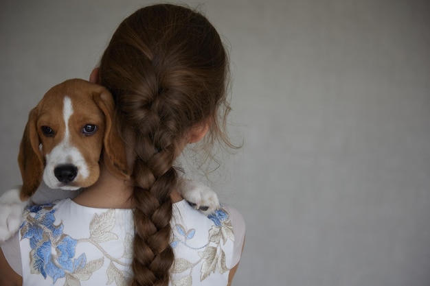 Dorso di una bambina con una lunga treccia e un cucciolo di beagle sulla spalla