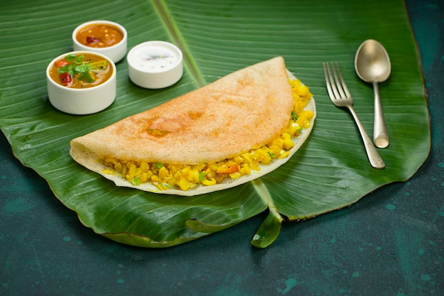 Dosa Masala dosafamoso articolo per la colazione dell'India meridionale realizzato in padella di ghisa in modo tradizionale e disposto su una foglia di banana fresca con sfondo verde scuro isolato