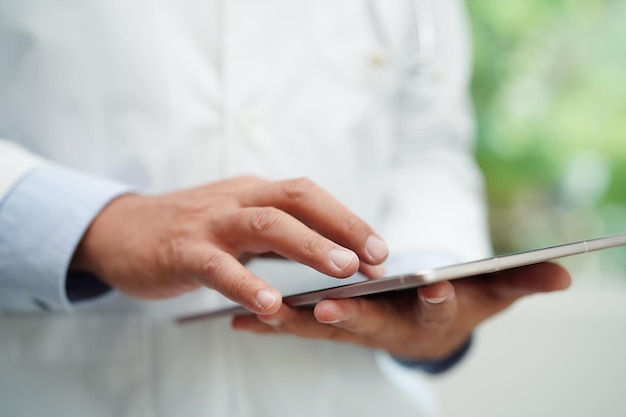 Dottore asiatico che usa un tablet per leggere il rapporto del paziente, controllare e cercare