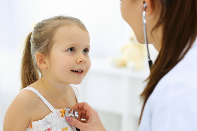 Dottore che esamina una ragazzina con lo stetoscopio. Paziente bambino felice e sorridente all'ispezione medica abituale. Concepti di medicina e assistenza sanitaria.