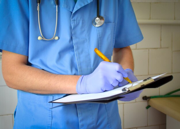 Dottore con uno stetoscopio sul collo e una scrittura uniforme blu su una prescrizione in bianco