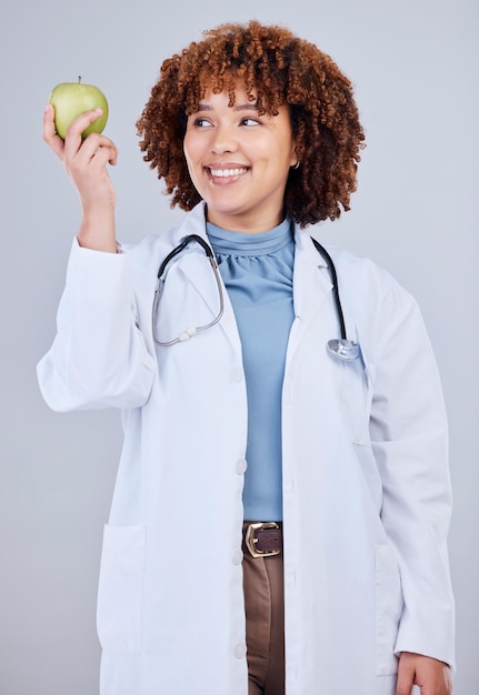 Dottore donna e sorriso con mela sullo sfondo bianco studio e vitamina c benessere felice donna operatrice medica nutrizionista e consigli di frutta verde per la nutrizione cibo sano e dieta di disintossicazione