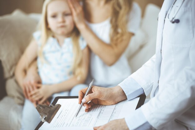 Dottore e paziente. Pediatra che utilizza appunti mentre esamina la bambina con sua madre a casa. Bambino malato e infelice all'esame medico. Concetto di medicina.