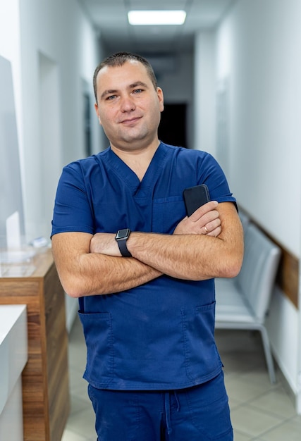 Dottore in abiti blu in posa davanti alla telecamera con le braccia incrociate. Medico in piedi vicino alla sala operatoria. Vista verticale