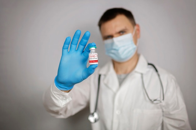 Dottore in maschera medica e guanti che tengono fiala e siringa con vaccino contro il coronavirus