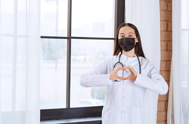 Dottore in maschera nera con uno stetoscopio in piedi vicino alla finestra e l'invio di amore.