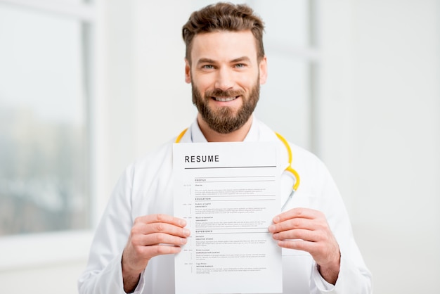 Dottore in uniforme che tiene curriculum per l'assunzione di lavoro nell'interno bianco. Immagine focalizzata sulla carta e sulle mani