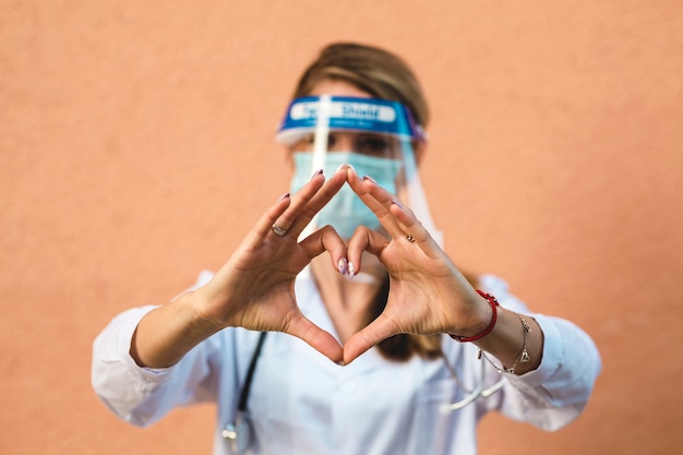 Dottoressa con maschera facciale. Primo piano della mano con forma di cuore.