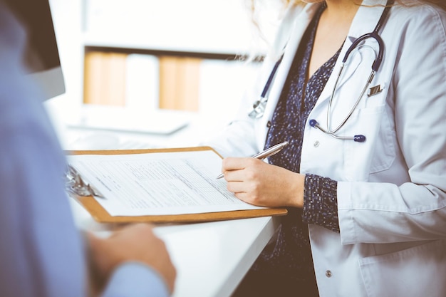 Dottoressa e paziente maschio che discutono dell'attuale esame sanitario mentre sono seduti in clinica, primo piano. Concetto di medicina.