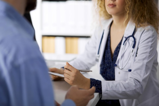 Dottoressa e paziente maschio che discutono dell'attuale esame sanitario mentre sono seduti in clinica, primo piano.