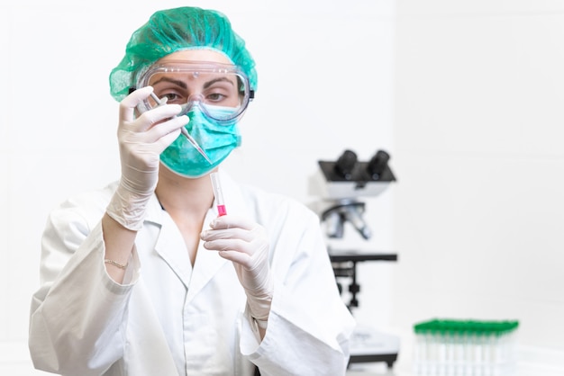 Dottoressa in laboratorio con una provetta per l'analisi del sangue e il campionamento del coronavirus al microscopio.