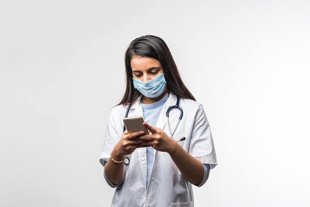 Dottoressa indiana che parla su smartphone Eccitata, indossa una maschera medica nella pandemia di coronavirus