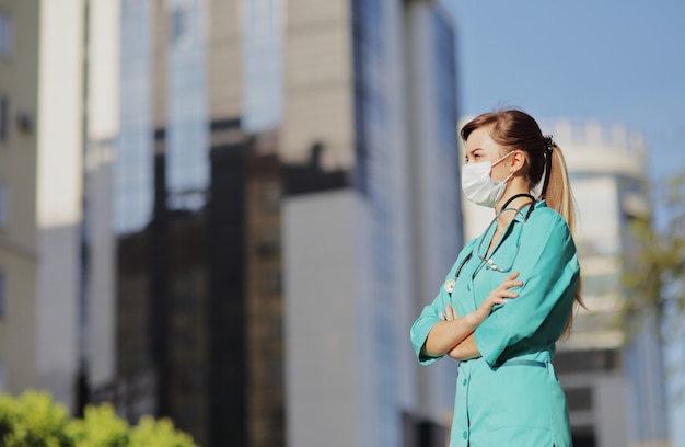 Dottoressa, infermiera che indossa una maschera protettiva in città. Grattacielo, cielo