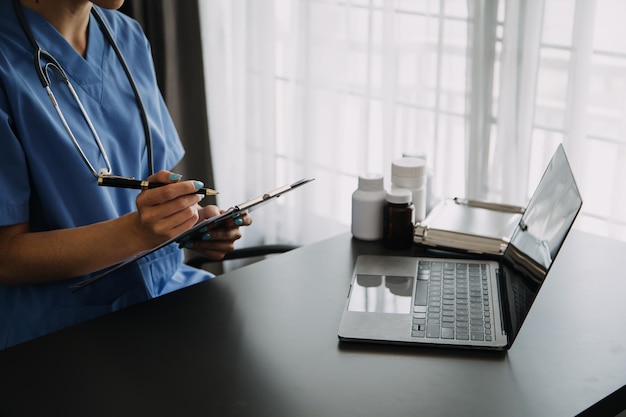 Dottoressa seria che utilizza il computer portatile e scrive note nel diario medico seduto alla scrivania Medico medico professionista della giovane donna che indossa camice bianco e stetoscopio che lavora al computer sul posto di lavoro